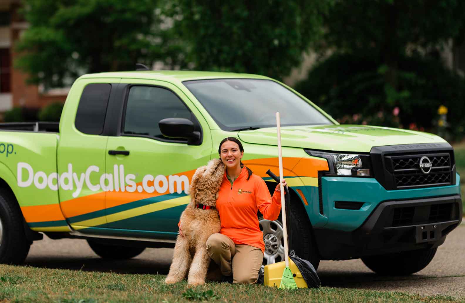 DoodyCalls franchise owner kneeling in front of truck with dog and pet waste removal tools