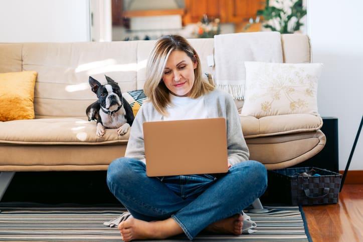 Young woman working from home with a boston terrier dog. DooyCalls businesswoman using laptop at sunny room.