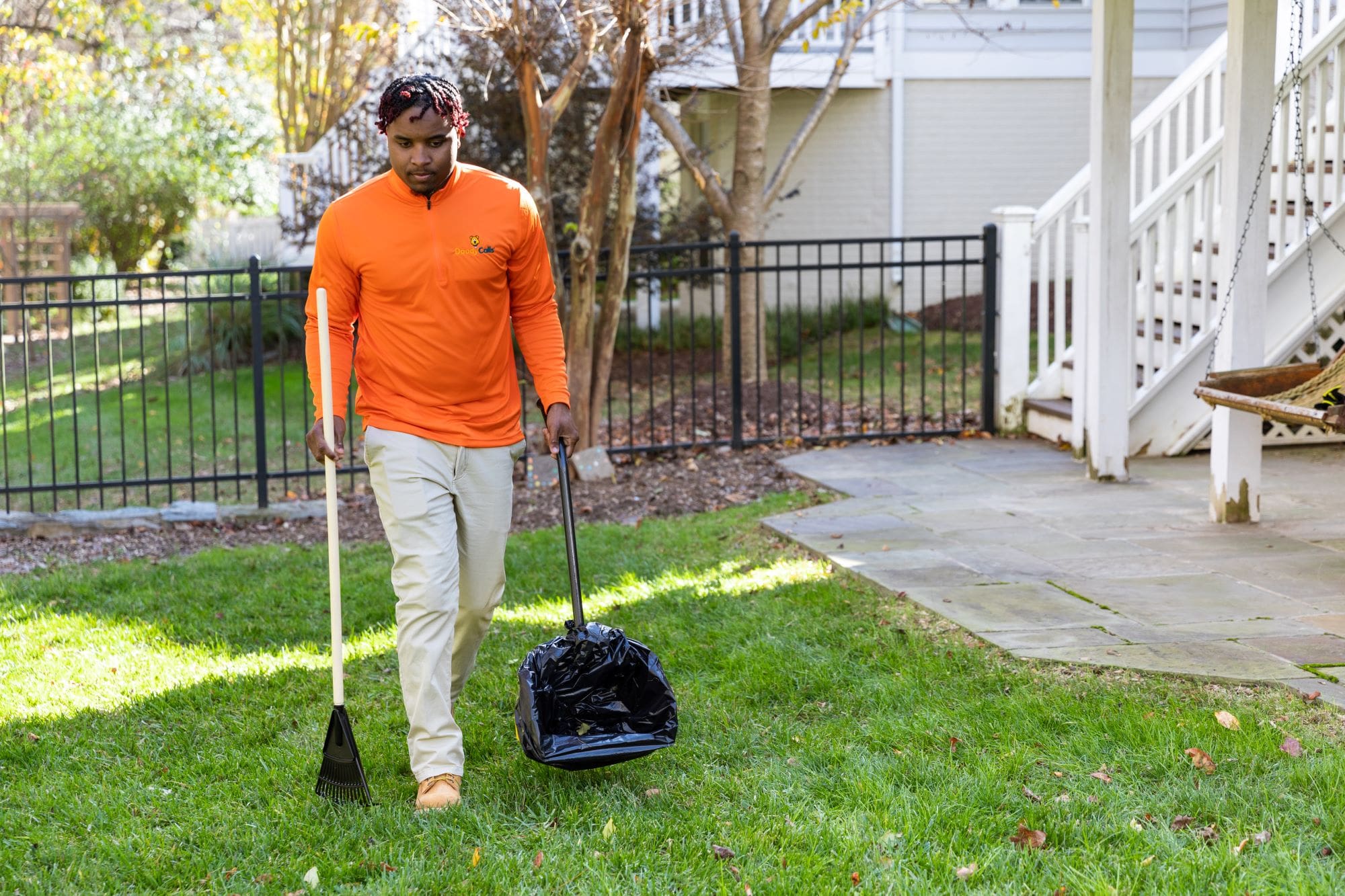 Dog poop cleaning service employee in branded DoodyCalls uniform scooping poop in a yard.